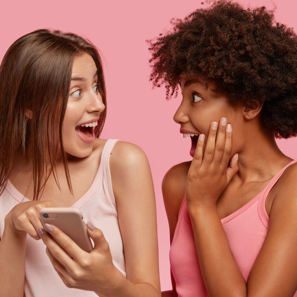 surprised-joyful-interracial-friends-look-happily-screen-cell-phone-read-something-unbelievable-pose-together-against-pink-wall-make-shopping-online-ethnicity-technology (1)